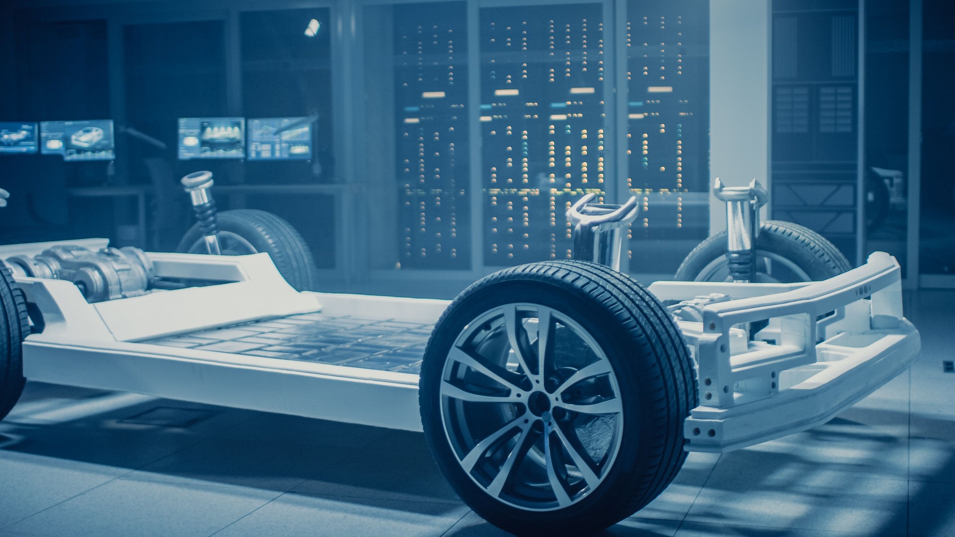 Automobile Engineers Discussing and Designing Electric Car Chassis Platform, Using Tablet Computers with 3D CAD Software. In Automotive Innovation Facility Vehicle Frame with Wheels, Engine and Battery